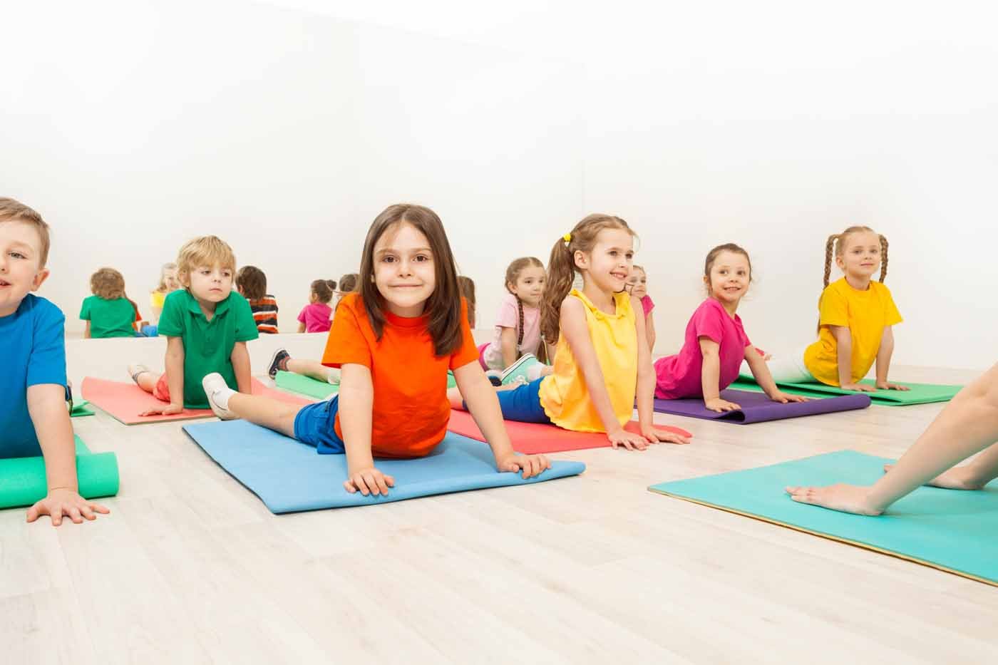 Group of happy kids, 5-6 years old boys and girls, stretching their backs on yoga mats during gymnastics in sports club
